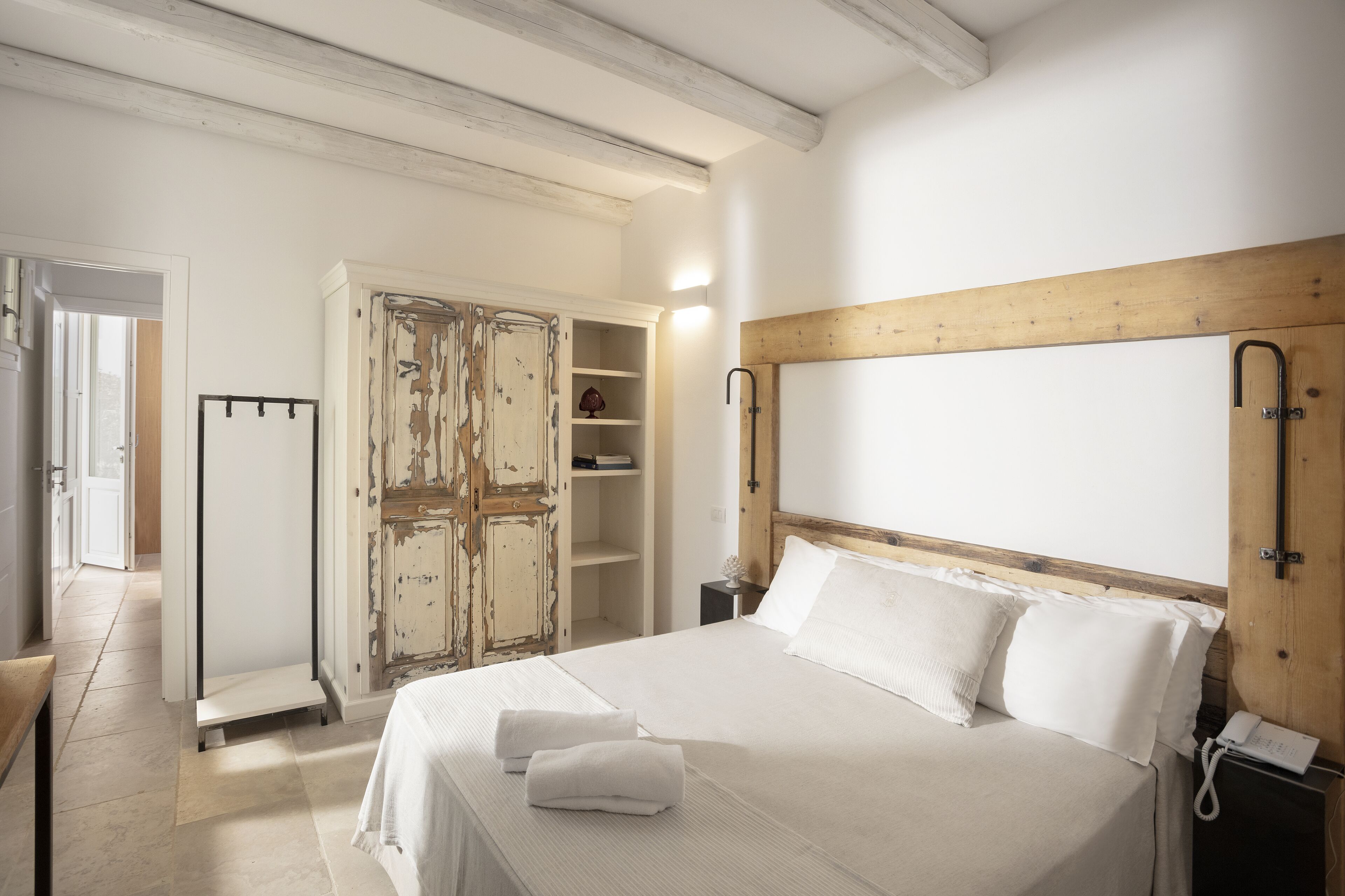 A bedroom with a large bed, a wooden headboard, a wardrobe, and a bedside table with a lamp.