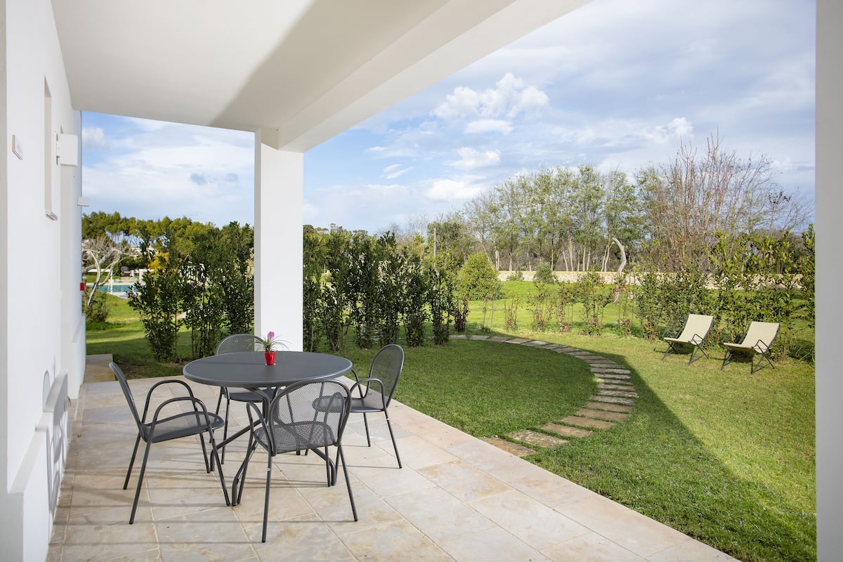 Une terrasse extérieure avec une table ronde et des chaises, entourée d’une pelouse bien entretenue et d’un chemin en pierre.