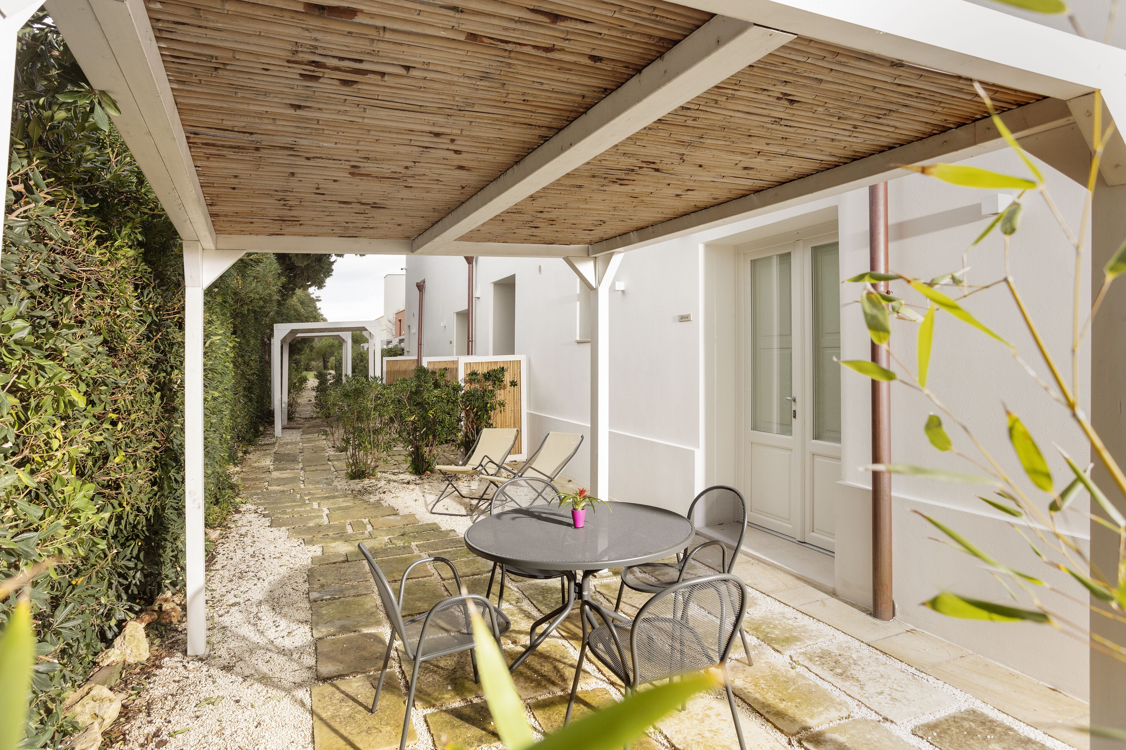 Une terrasse couverte avec un sol en pierre, une table ronde entourée de chaises et une plante en pot.