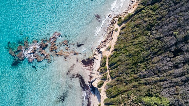 Vista aérea de una zona costera con aguas turquesas cristalinas, costa rocosa y vegetación verde exuberante.