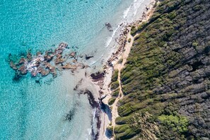 Vue aérienne d’une zone côtière avec des eaux turquoise limpides, un littoral rocheux et une végétation verdoyante et luxuriante.