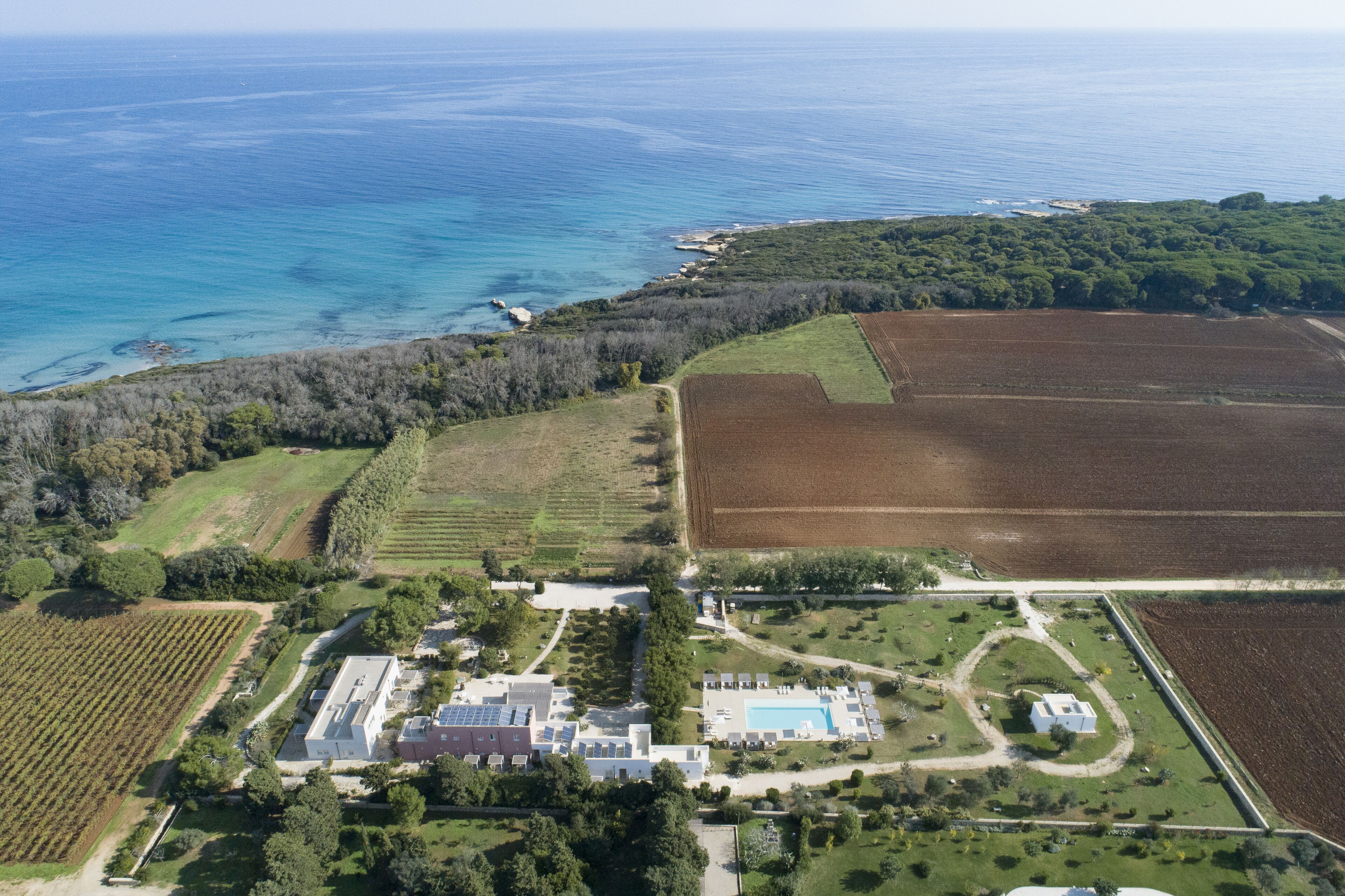 An aerial view of a coastal property with fields, a swimming pool, and a large building with solar panels.