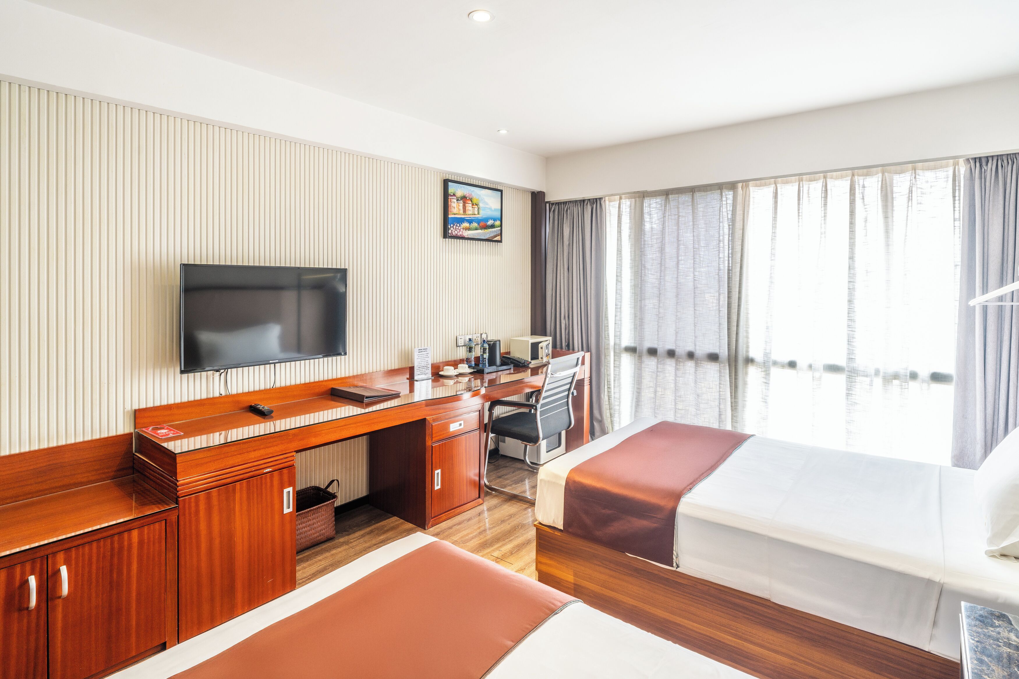 Habitación de hotel con un escritorio de madera, televisión, cama y un ventanal con cortinas.