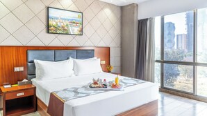 A hotel room with a large bed, a nightstand, a painting on the wall, and a view of the city through the window. - Swiss Lenana Mount Hotel (Nairobi)