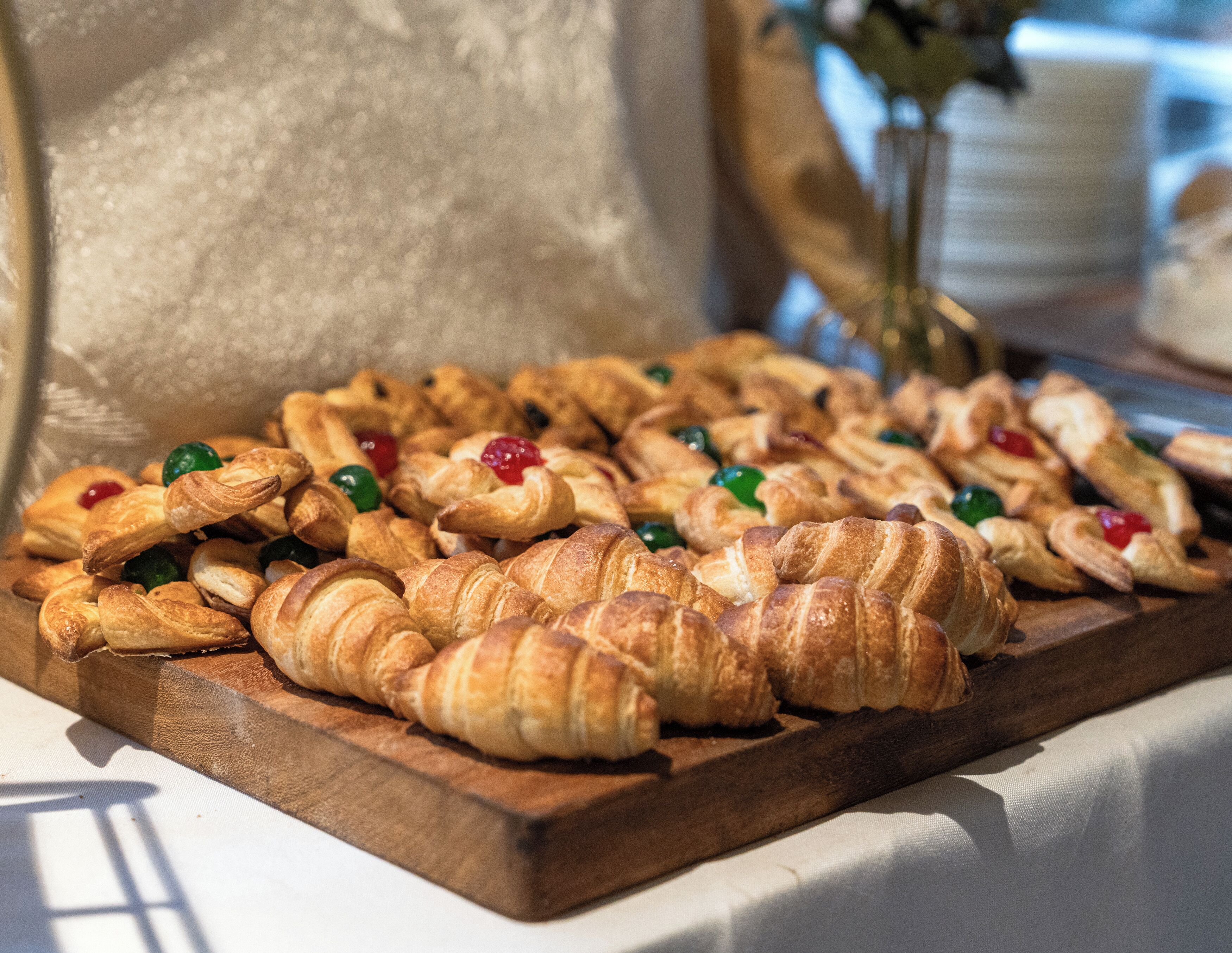 A wooden board with assorted pastries, including croissants and pastries with fruit toppings.