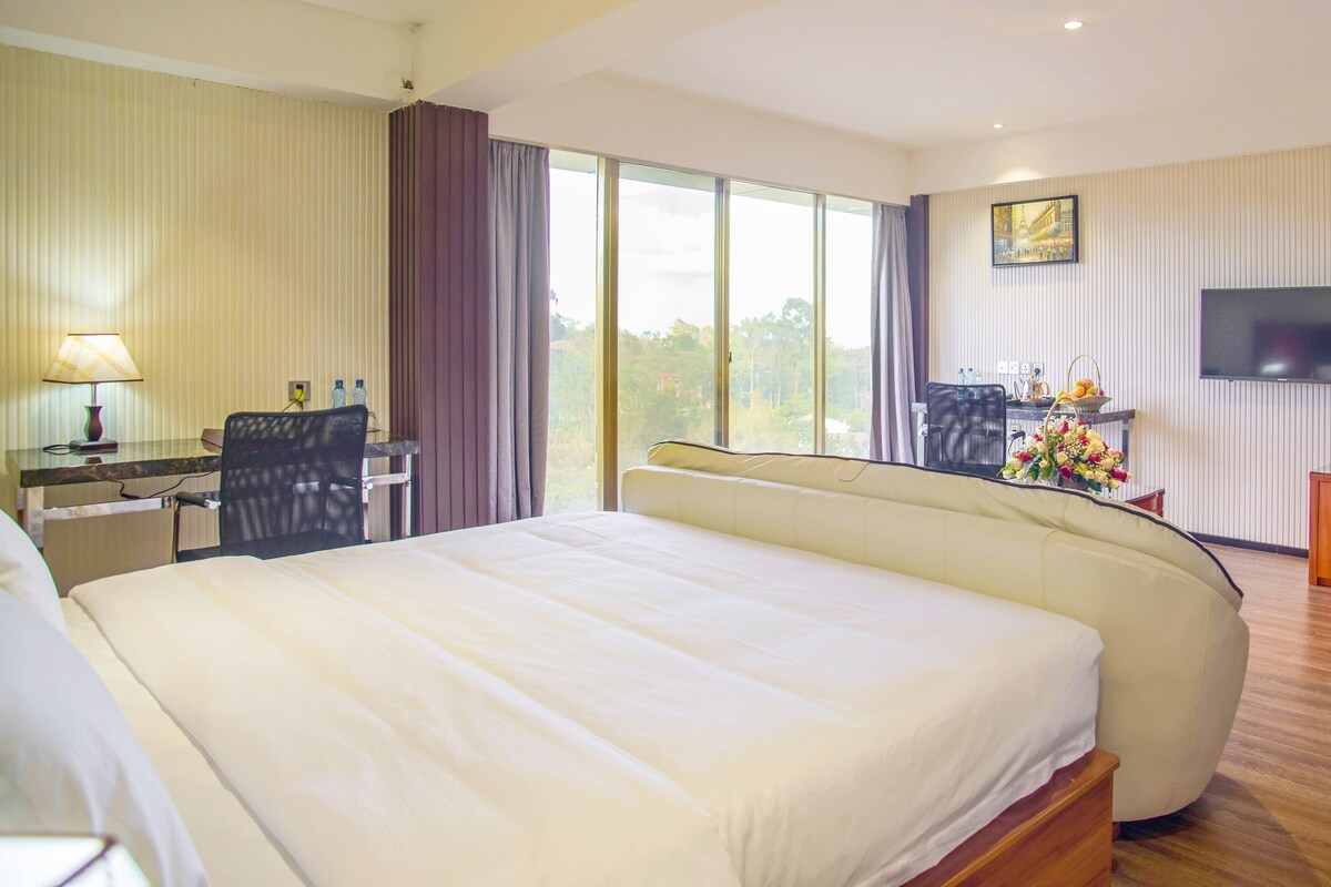 A hotel room with a large bed, a desk with a lamp, a television, and a view of the outdoors.