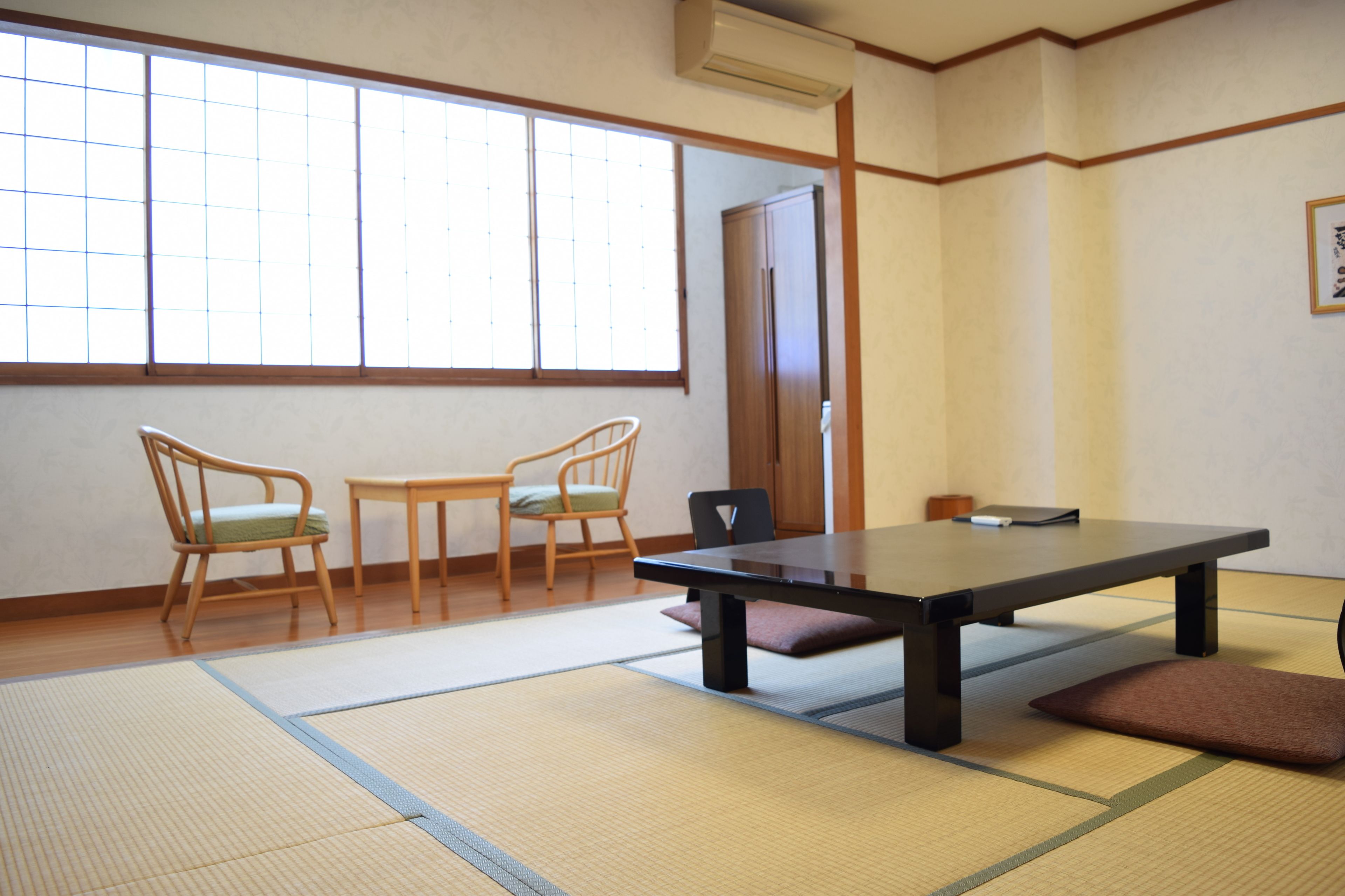 A traditional Japanese room with tatami flooring, a low table, and two chairs.
