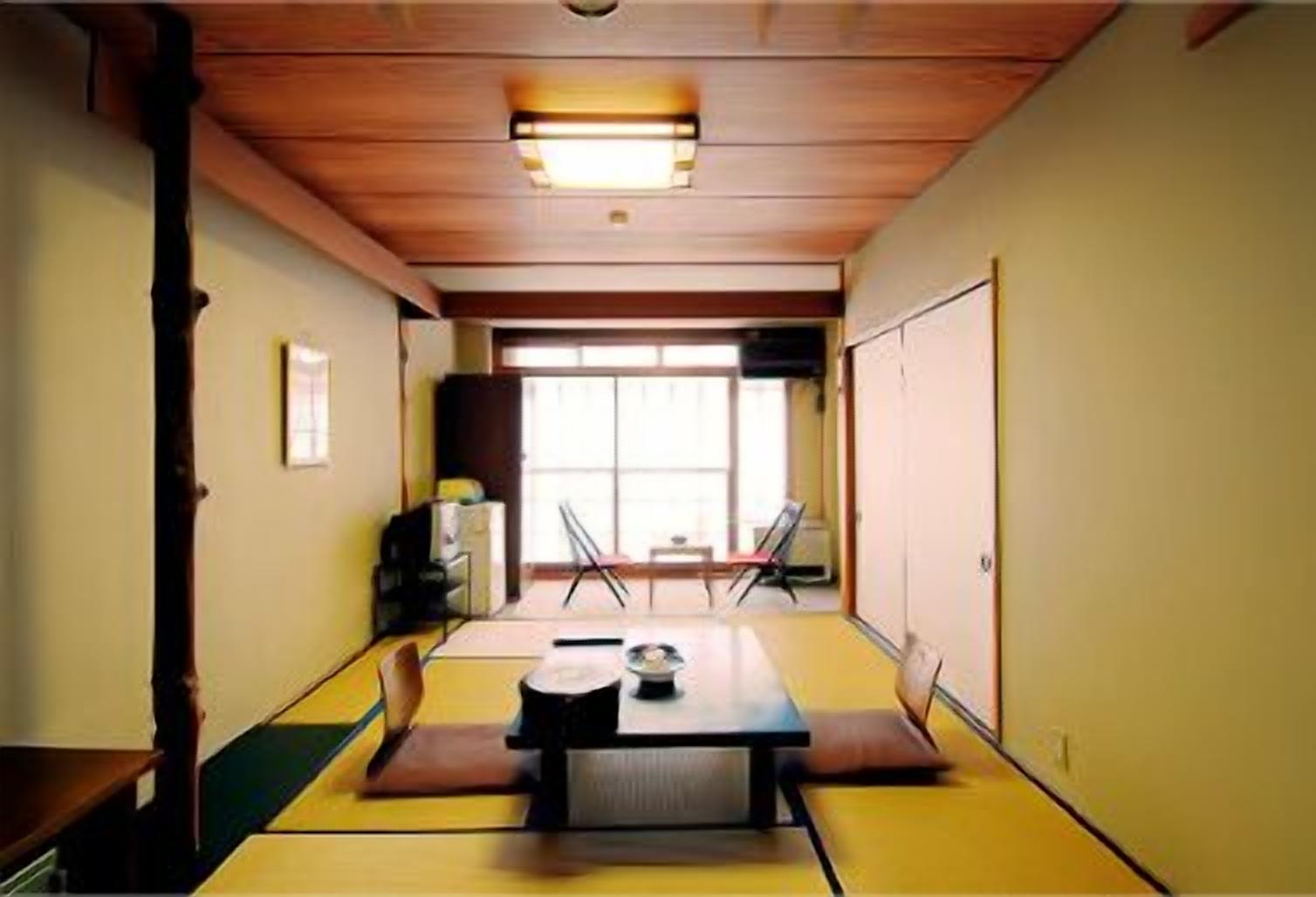 Una habitación tradicional japonesa con suelo de tatami, una mesa baja con cojines y puertas correderas.