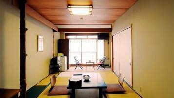 Una habitación tradicional japonesa con suelo de tatami, una mesa baja con cojines y puertas correderas.