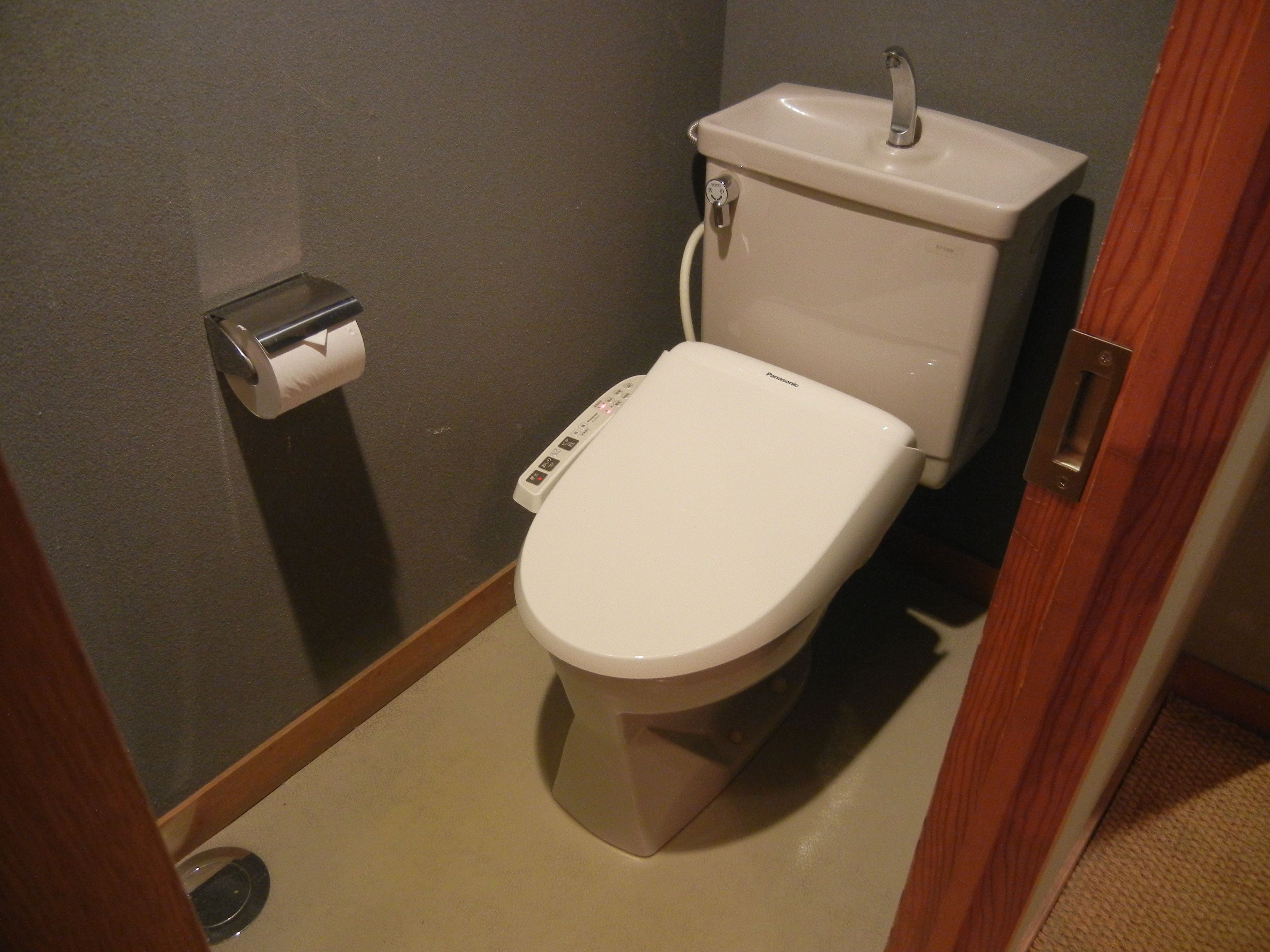 A standard toilet with a control panel, a toilet paper holder, and a sink with a faucet.