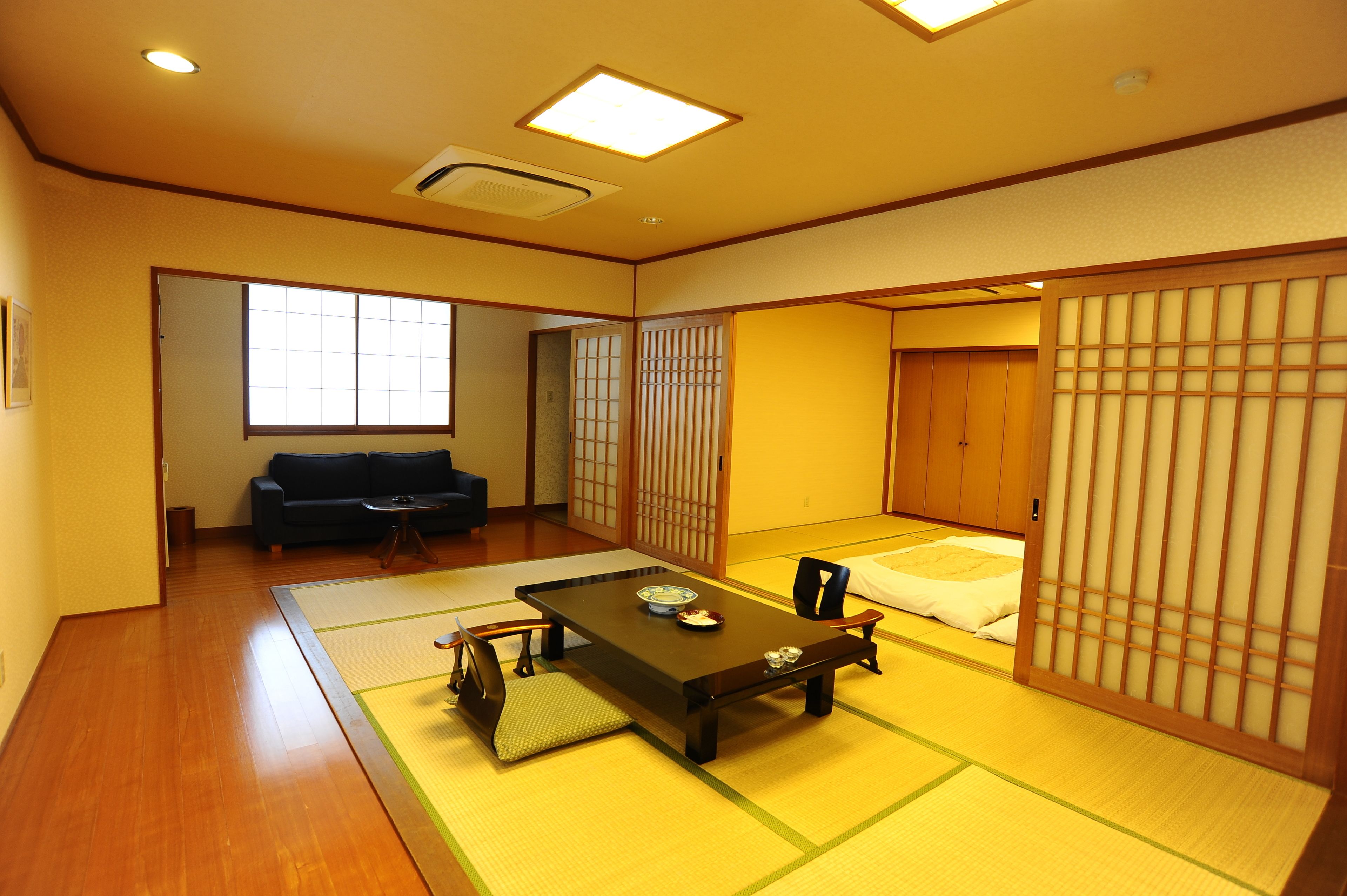 A traditional Japanese room with tatami flooring, a low table with cushions, a sofa, and sliding doors.