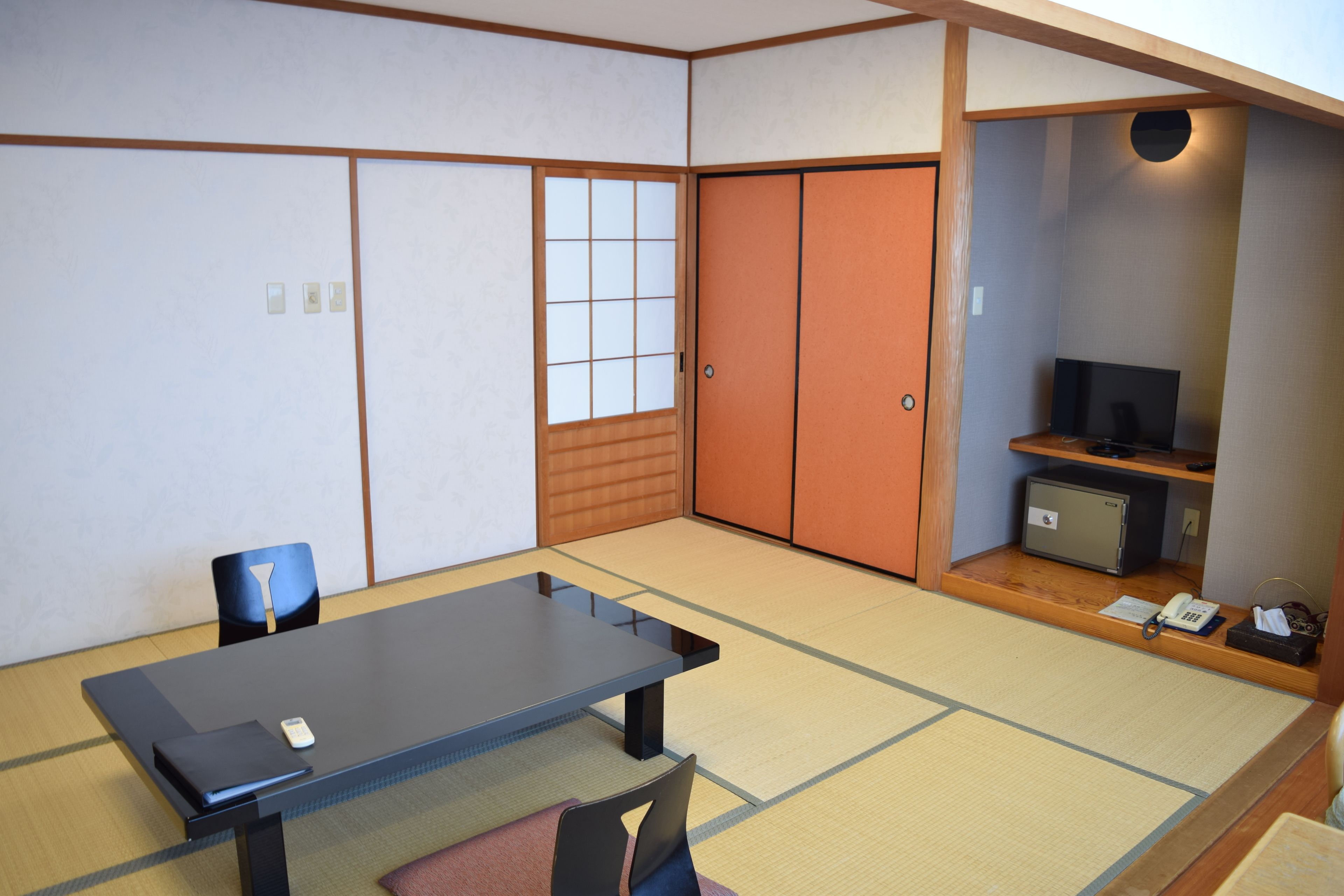 Een traditionele Japanse kamer met tatami vloerbedekking, een lage tafel, een stoel, schuifdeuren, een televisie en een klein kluisje.