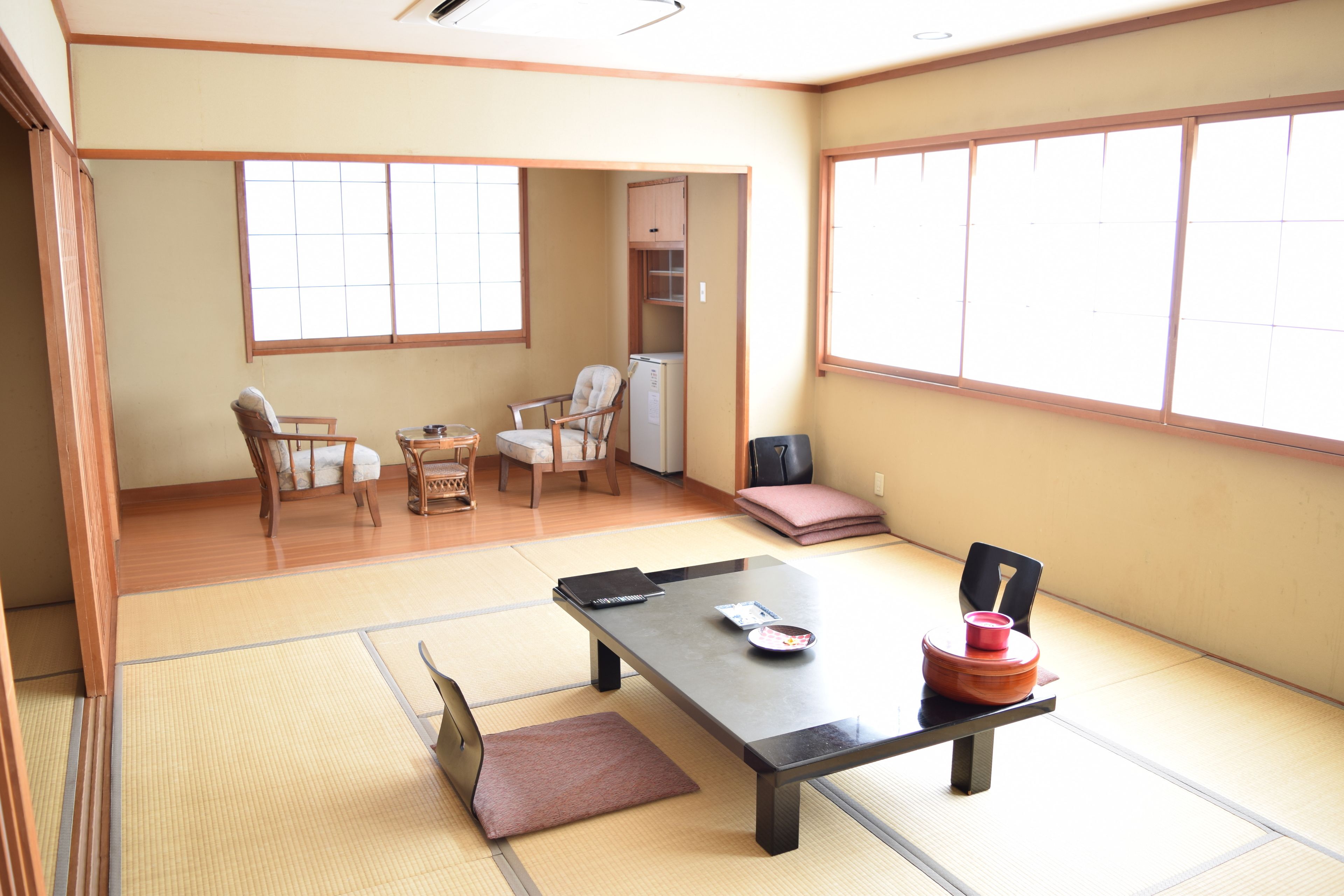 A traditional Japanese room with tatami flooring, a low table, chairs, and a sliding door leading to a kitchen area.