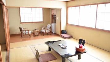 A traditional Japanese room with tatami flooring, a low table, chairs, and a sliding door leading to a kitchen area.