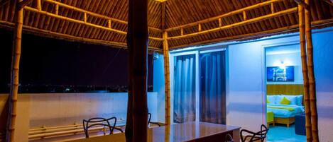 A room with a bamboo ceiling, a bed with a yellow pillow, and a view of the city at night.
