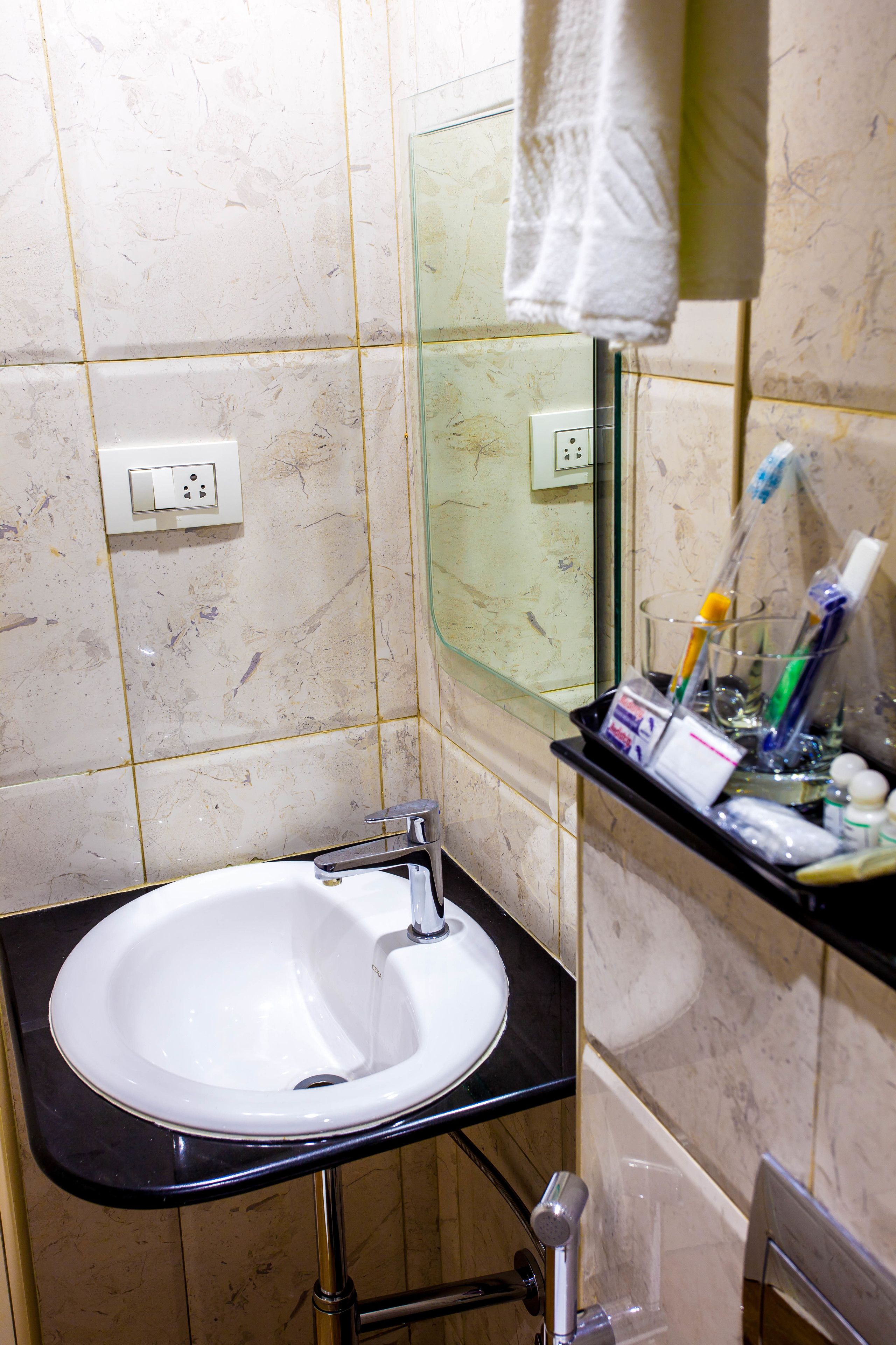 Un baño con lavamanos blanco, cabina de ducha de vidrio y repisa con artículos de aseo.