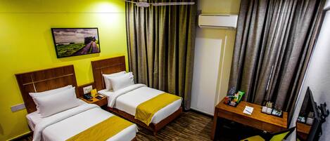 A hotel room with two beds, a desk, a chair, an air conditioner, and a painting on the wall.