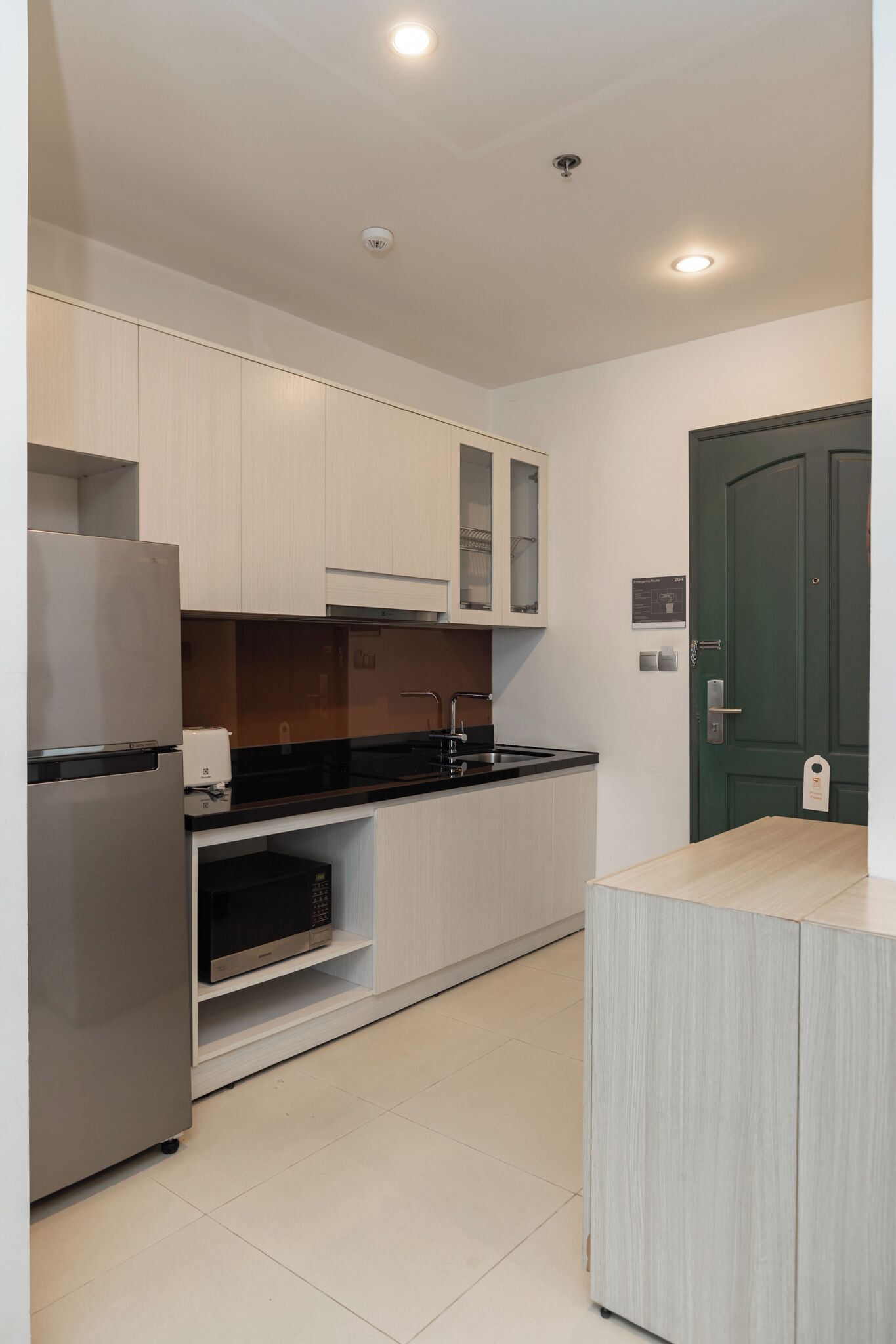 A modern kitchen with white cabinetry, a stainless steel refrigerator, a microwave, and a black countertop.