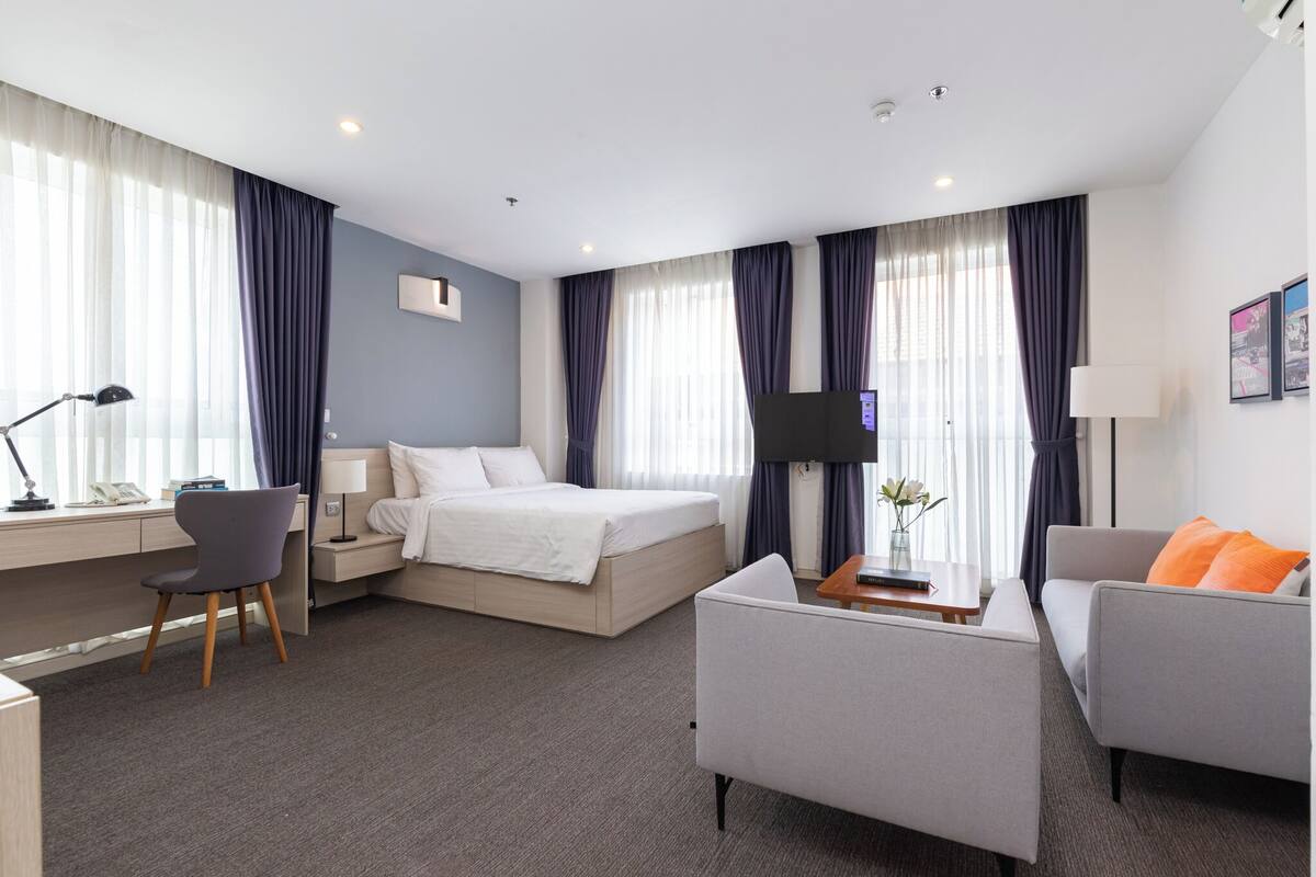 A modern hotel room with a bed, a desk, a sofa, and a TV.