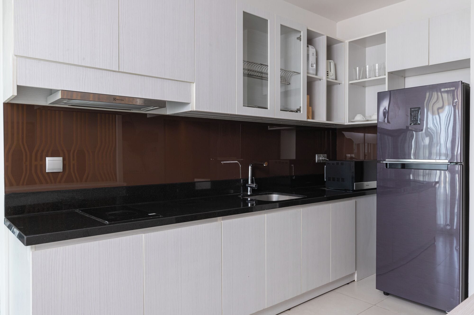 Cozinha moderna com armários brancos, geladeira de aço inoxidável e bancada preta.