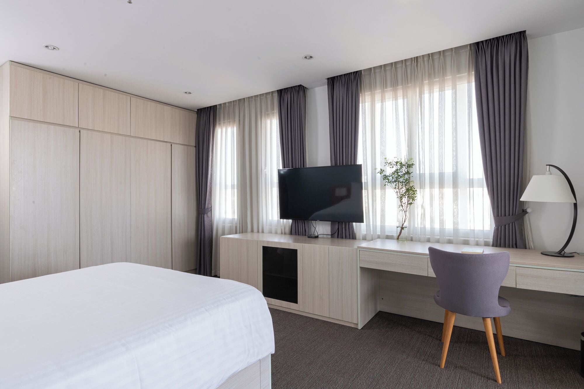 A hotel room with a bed, a desk with a TV, a chair, and a lamp.