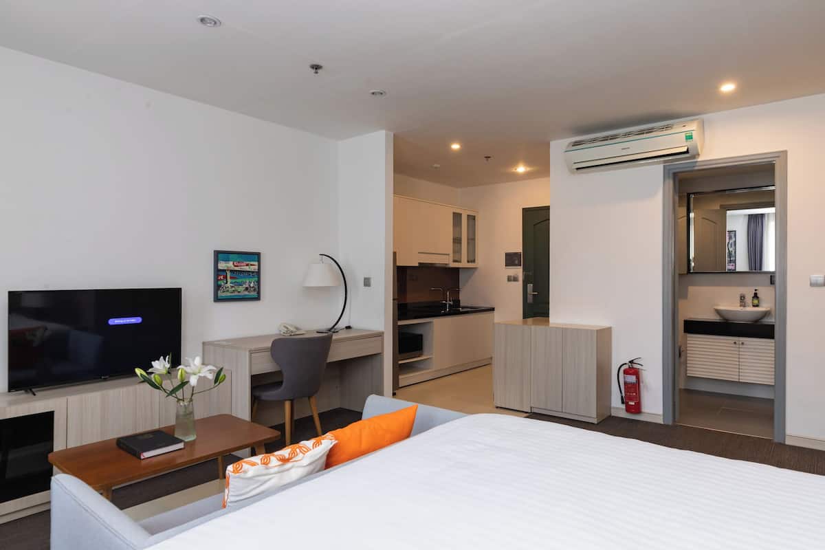 A modern hotel room with a bed, TV, desk, chair, and kitchenette.