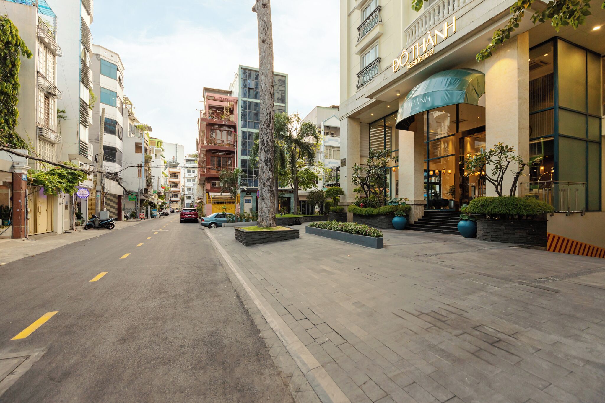 Un hotel moderno con una entrada destacada, un área exterior bien cuidada con macetas y una calle despejada al frente.