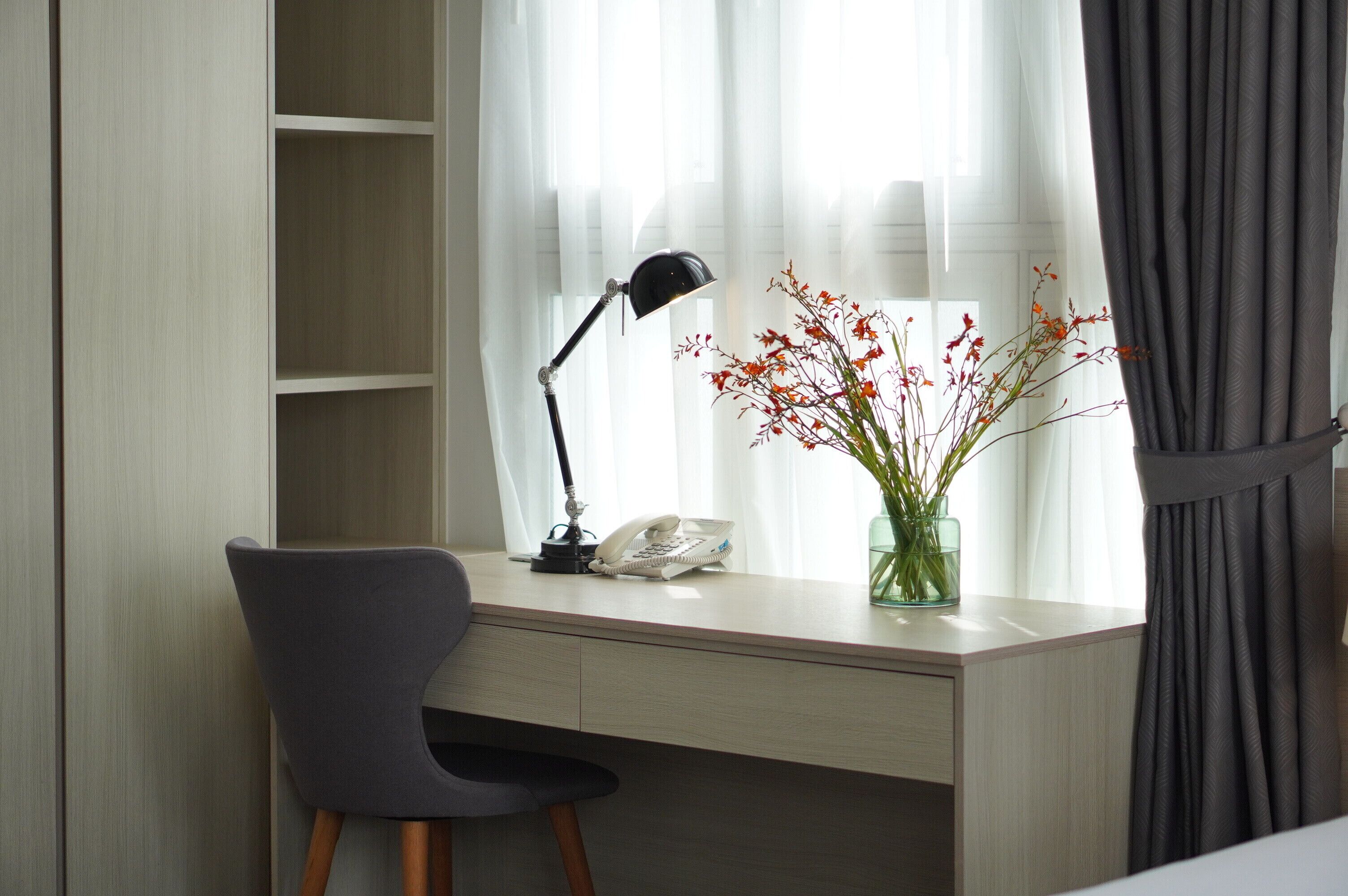 A desk with a lamp, a phone, and a vase with flowers.