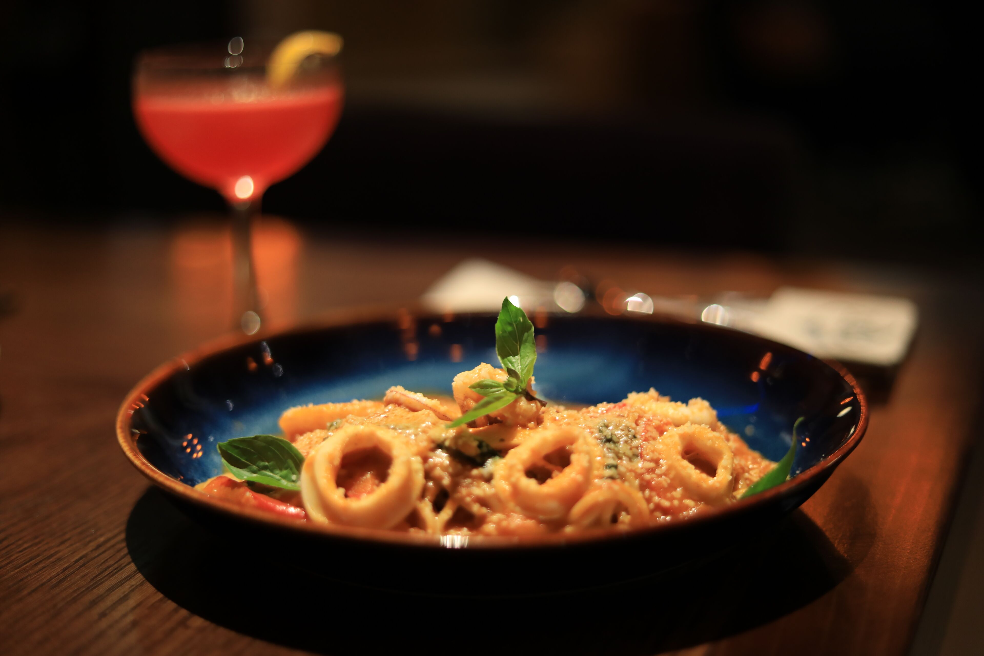 Een bord pasta met een rood drankje op de achtergrond.