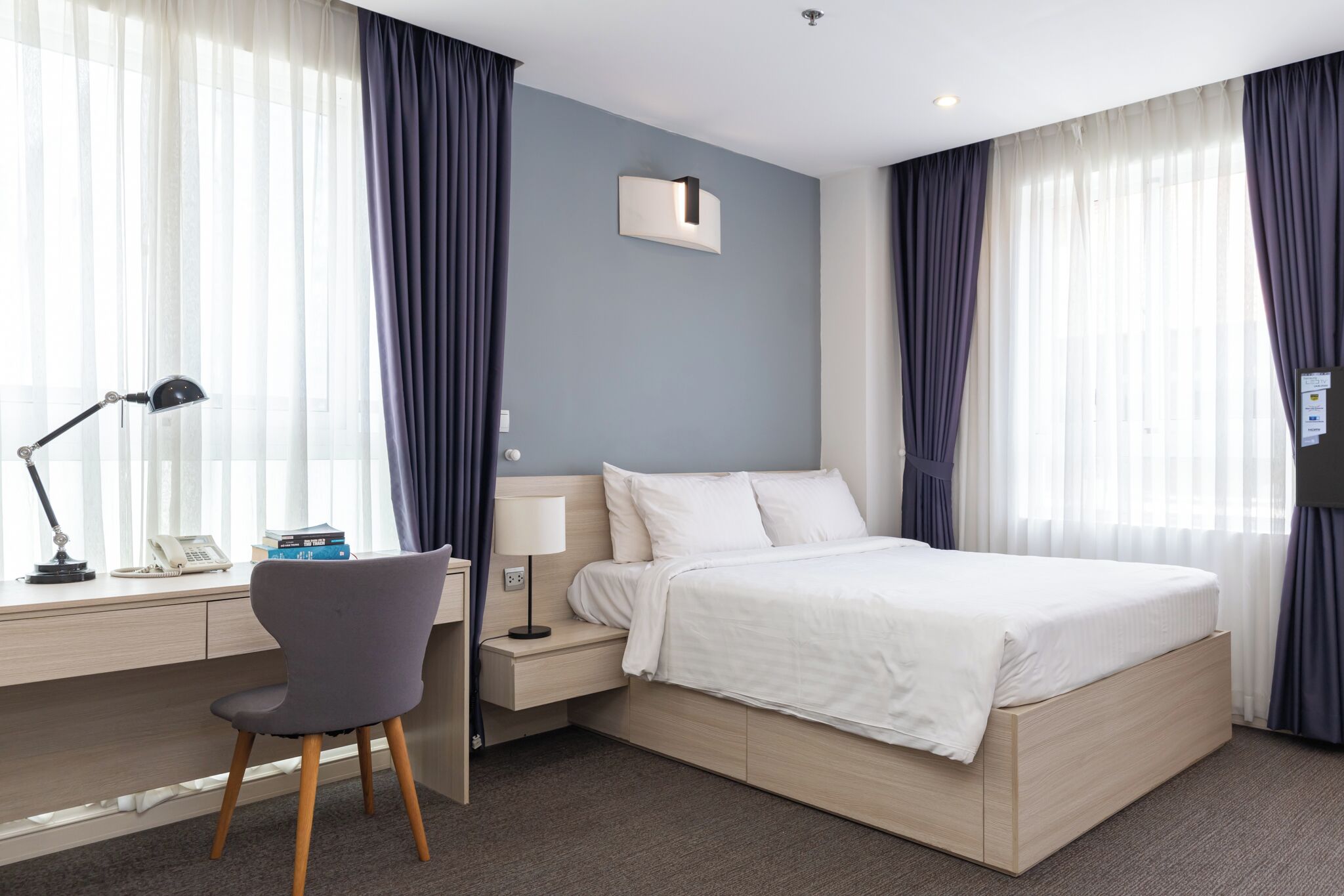 Une chambre d’hôtel comprenant un lit, un bureau avec une chaise, une lampe et une table de chevet.