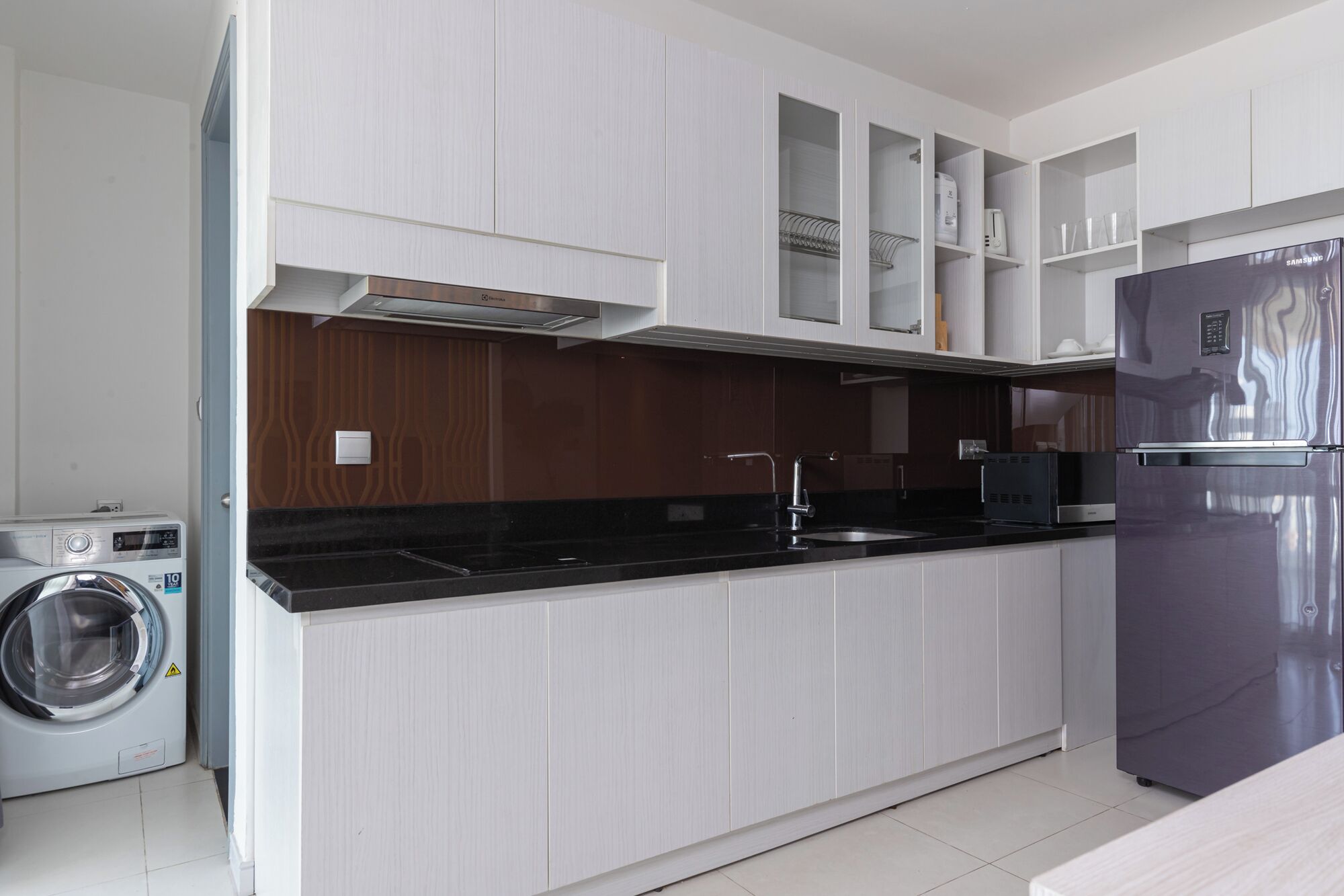 Cozinha moderna com máquina de lavar embutida, frigorífico de aço inoxidável e bancada preta.