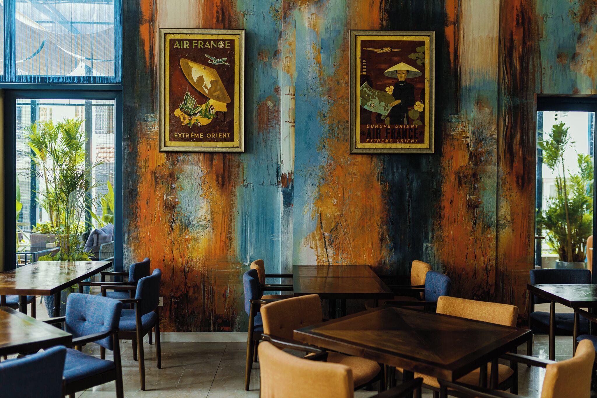 A restaurant interior with rustic wooden walls, framed posters, and a mix of blue and brown chairs.