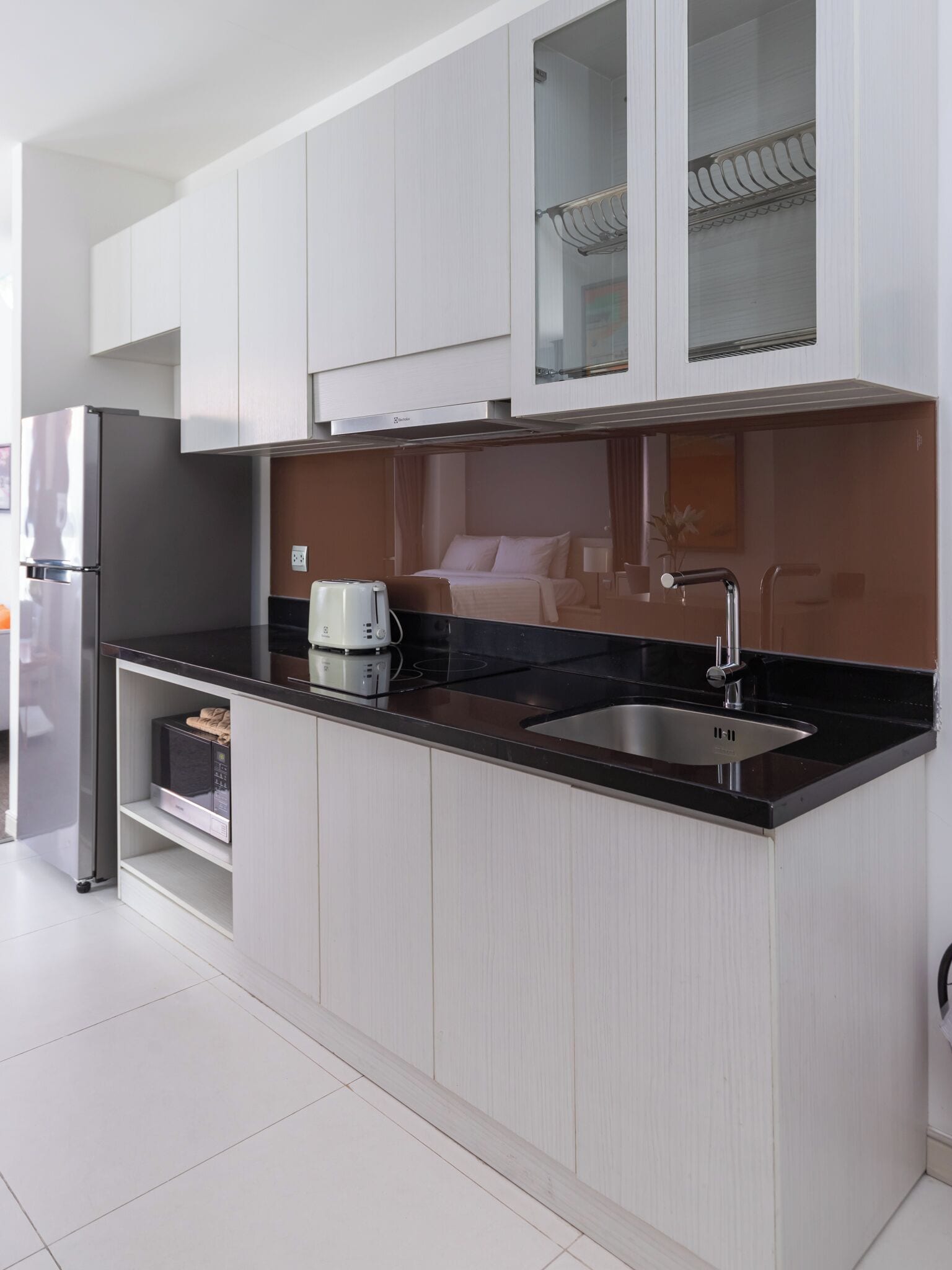 Une cuisine moderne avec des meubles blancs, un plan de travail noir, un évier en acier inoxydable et un micro-ondes encastré.