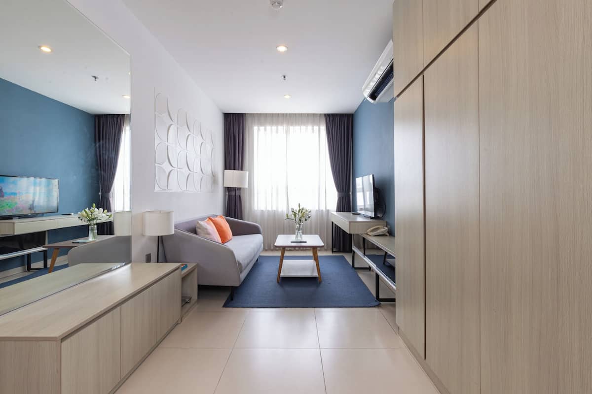 A modern hotel room with a sofa, a TV, a desk, and a large wardrobe.
