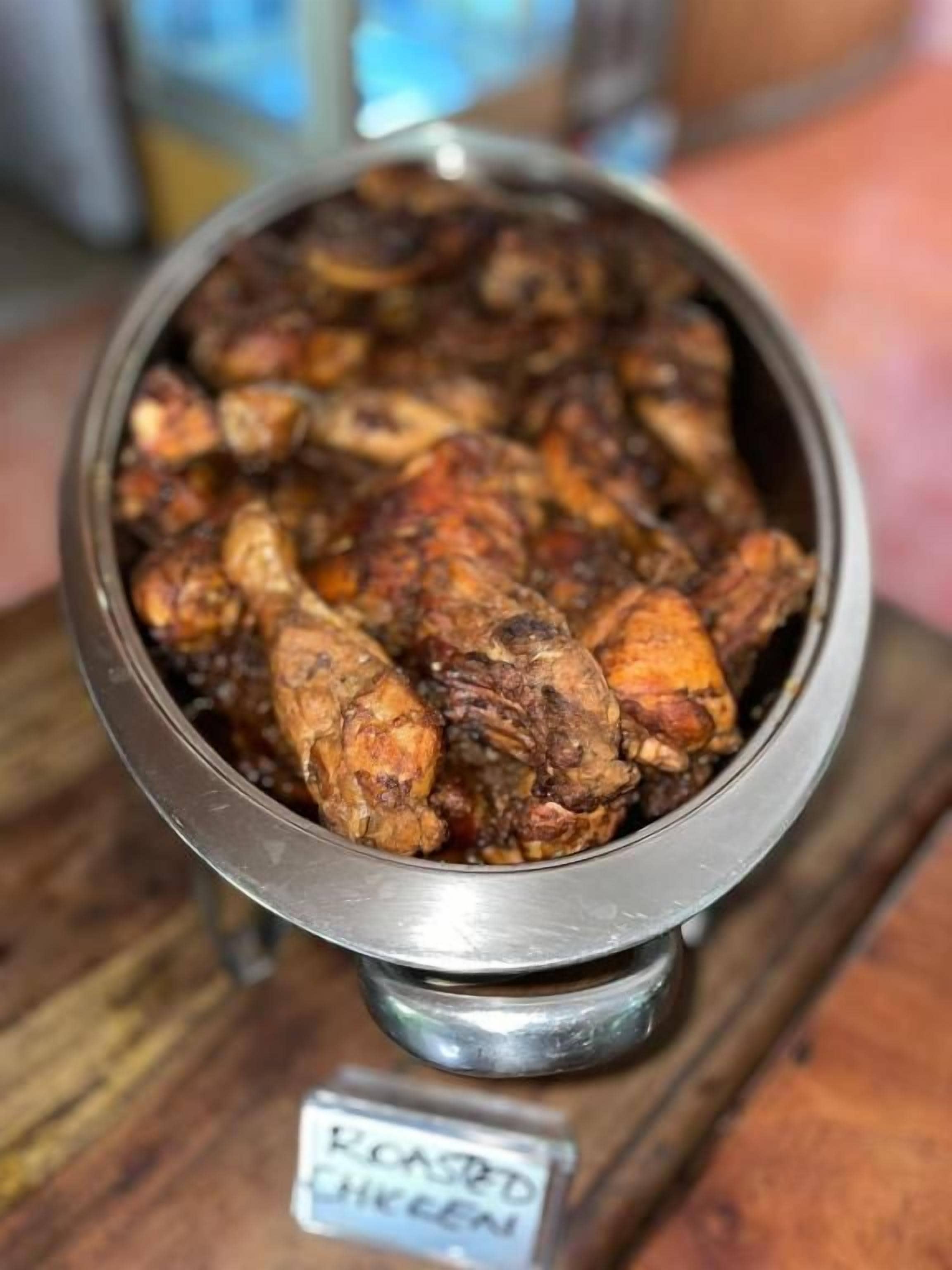 A metal bowl containing roasted chicken on a wooden surface.