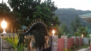Una entrada cerrada con muro de piedra y portón metálico, que da a un camino de entrada pavimentado.