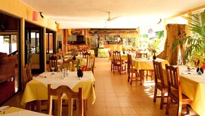 Un restaurante con varias mesas y sillas, una zona de recepción y una cocina visible al fondo.
