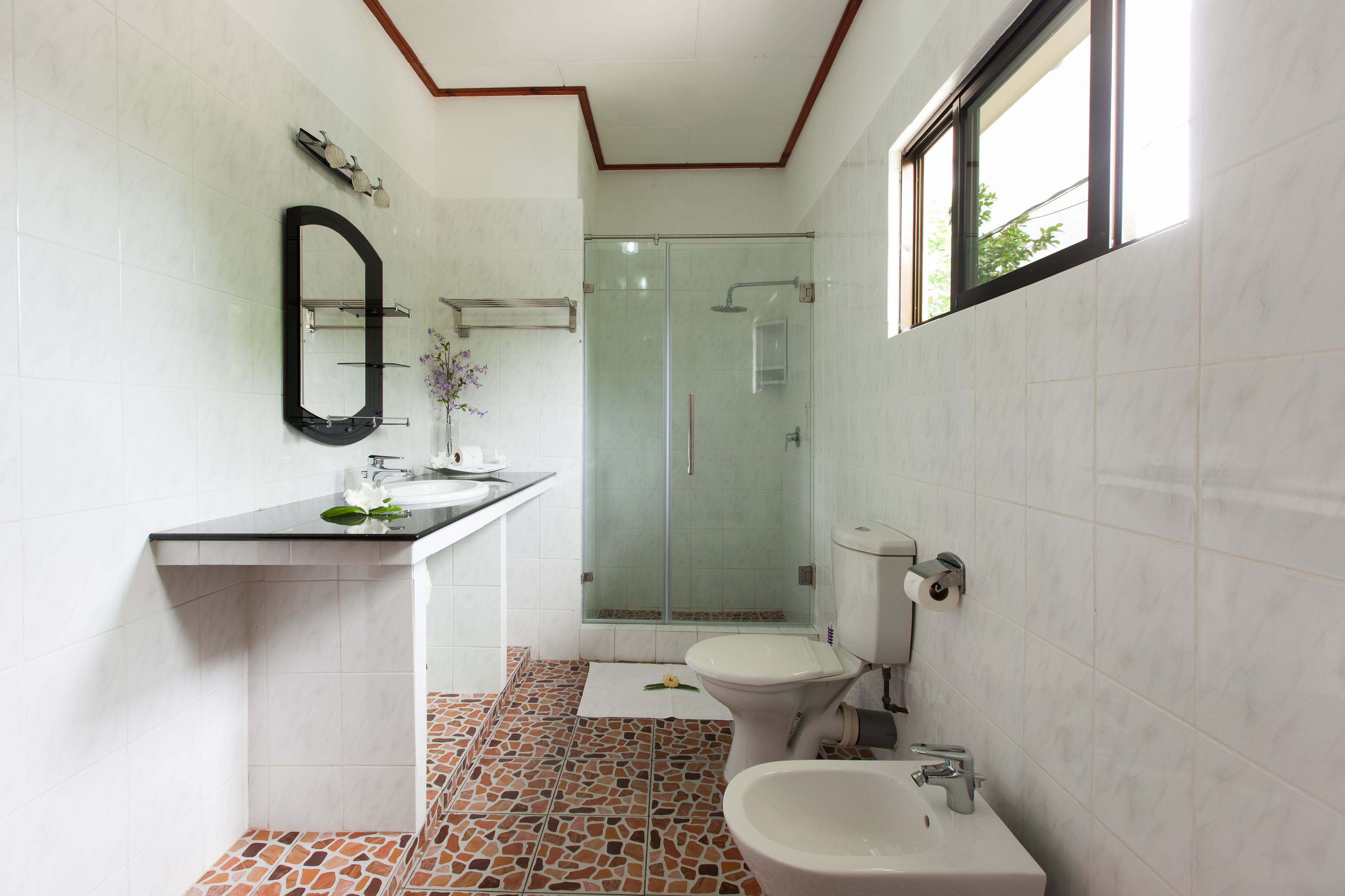 Une salle de bain moderne dotée d’une douche à parois de verre, de toilettes, d’un bidet et d’un lavabo avec un miroir au-dessus.