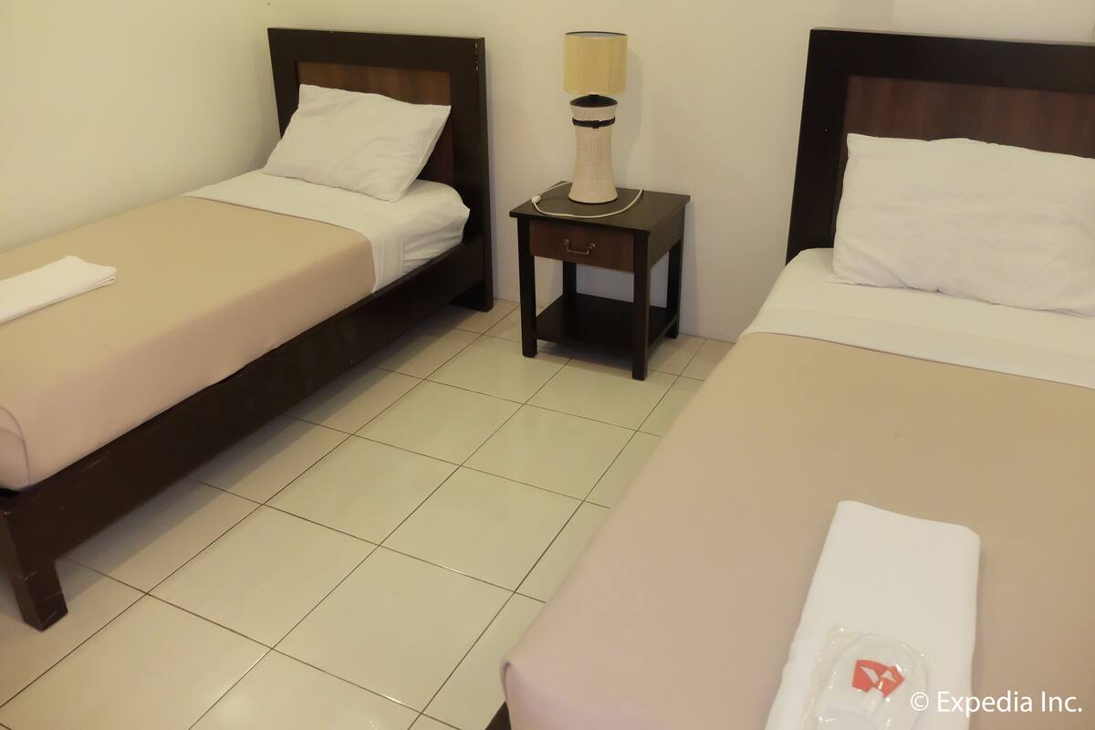 Hotellihuone, jossa on kaksi erillistä sänkyä, yöpöytä lampun kanssa ja laattalattia.