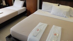 Zwei Hotelbetten mit weißen Laken, ein Holz-Kopfteil und ein Nachttisch mit Lampe und Telefon.