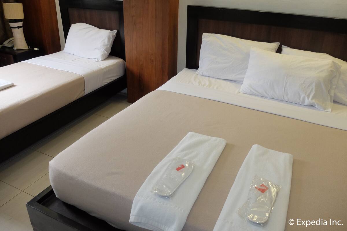 Kaksi hotellihuoneen sänkyä valkoisilla lakanoilla, puinen pääty ja yöpöytä, jossa on lamppu ja puhelin.