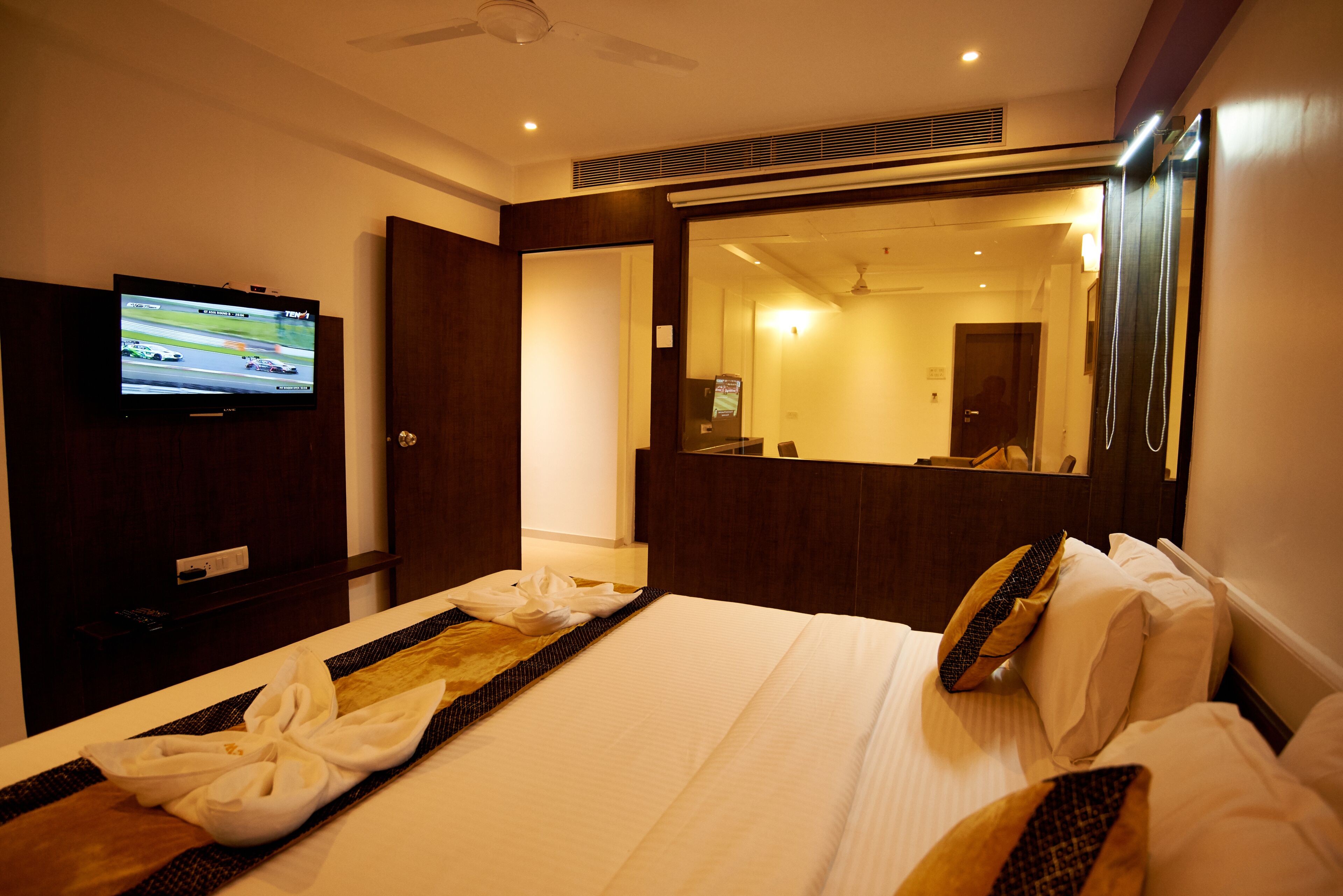 A hotel room with a bed, a television displaying a racing game, a mirror, and a door leading to another room.