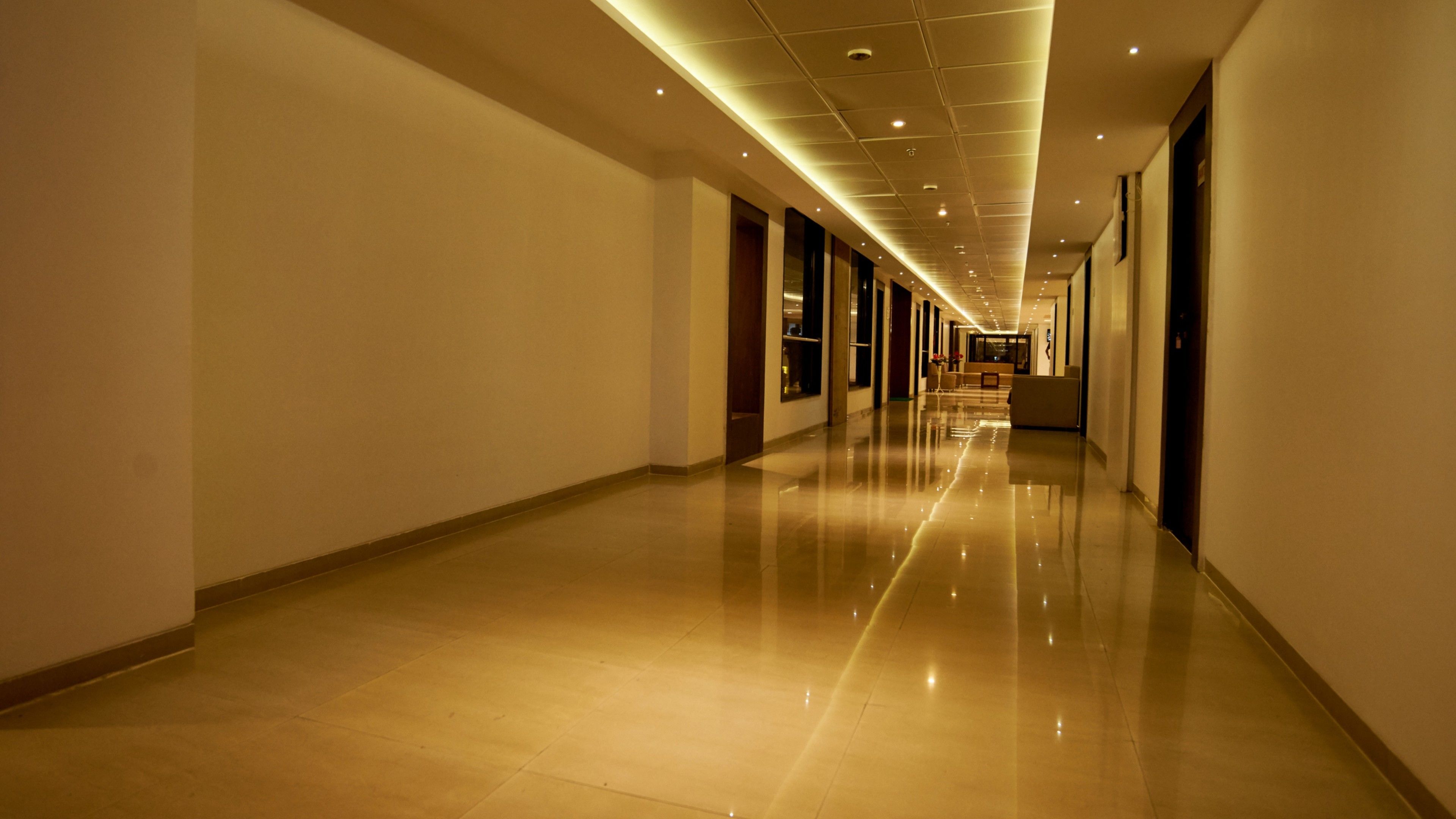 Un pasillo largo y bien iluminado con piso brillante, que conduce a una zona de estar con mesas y sillas.