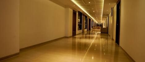 Un pasillo largo y bien iluminado con piso brillante, que conduce a una zona de estar con mesas y sillas.