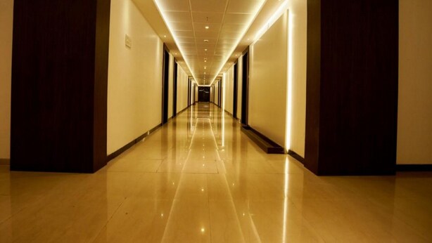 Un largo pasillo bien iluminado con piso brillante que conduce a una habitación oscura al final.