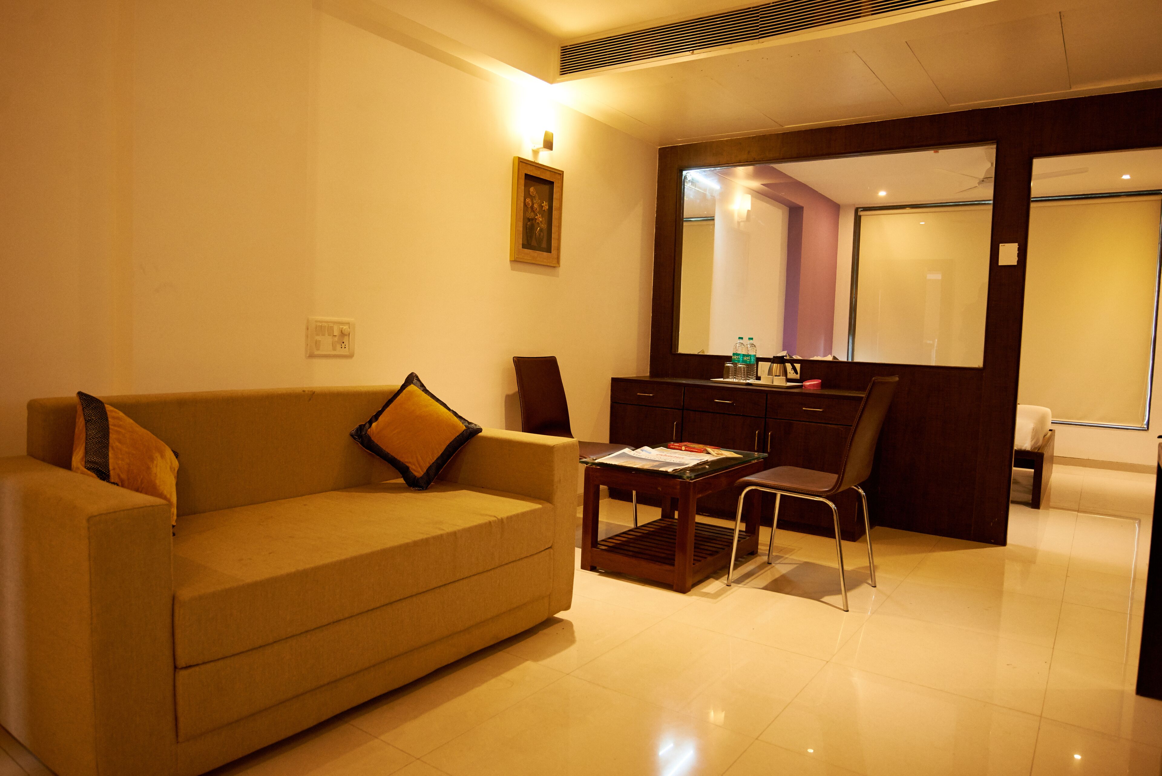 A modern living room with a sofa, a coffee table, and a chair. There is a wooden cabinet and a large mirror on the wall.
