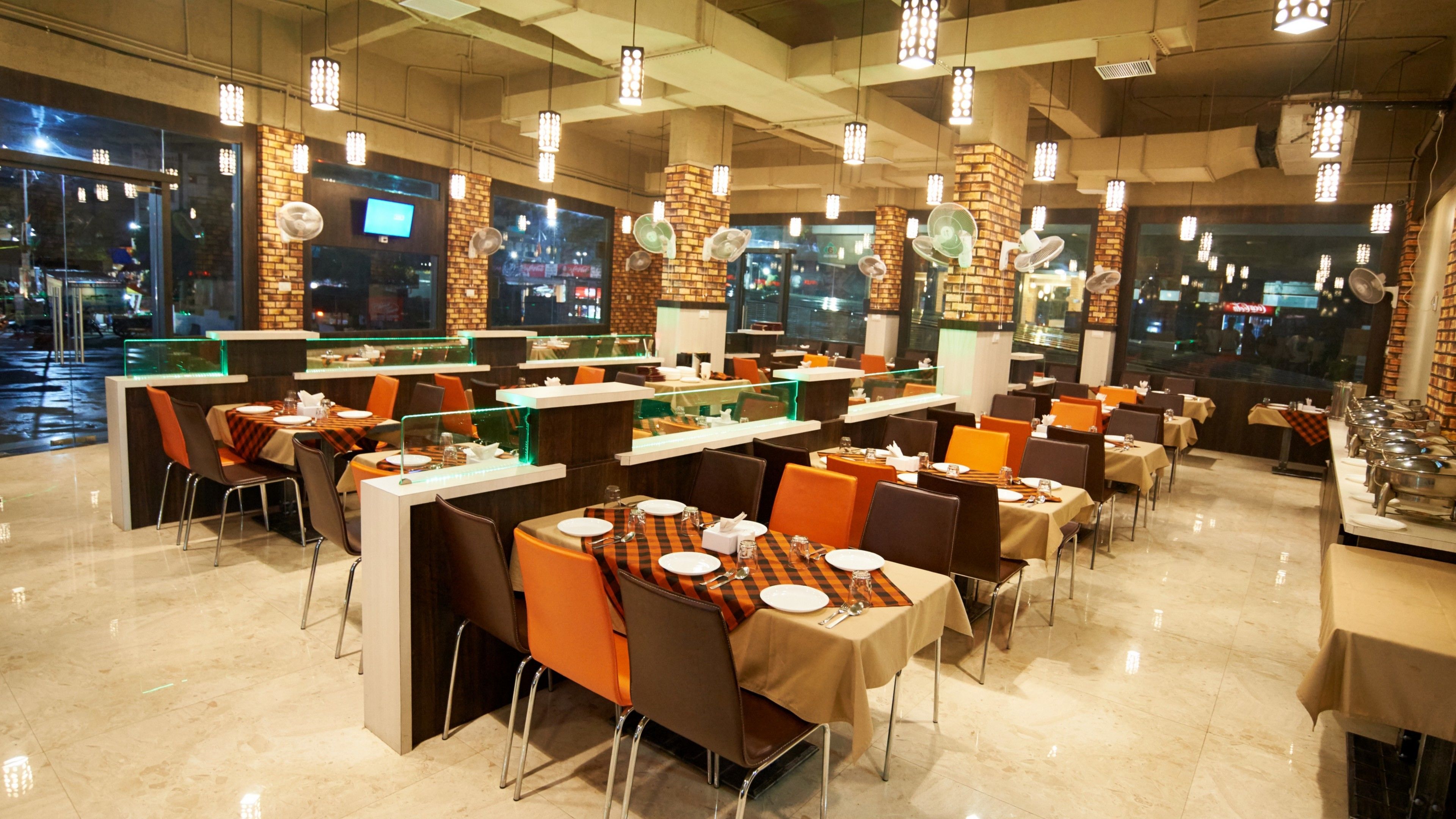 A modern restaurant with multiple dining areas, each with tables and chairs. There are large windows providing views of the cityscape.
