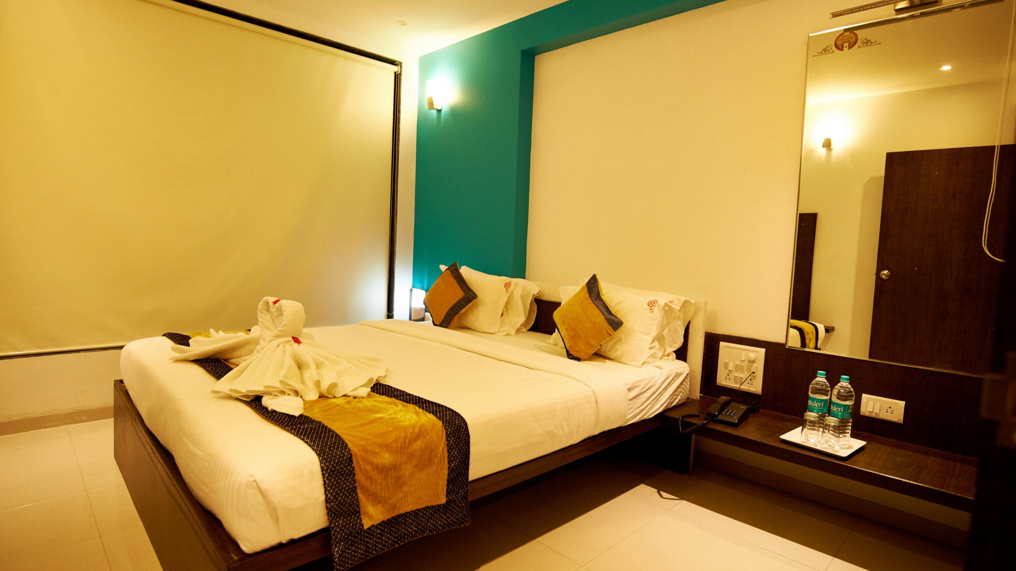 A hotel room with a bed, bedside table, and a mirror.