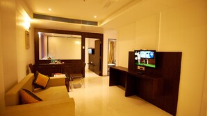 Una habitación de hotel moderna con una sala de estar que incluye un sofá, un televisor y un mueble de madera para entretenimiento.