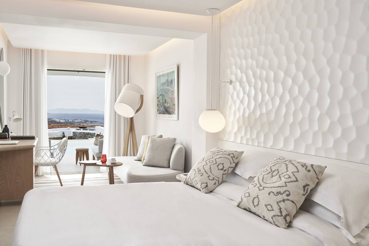 A modern hotel room with a large bed, a desk, a chair, and a view of the city.